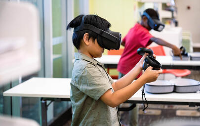 Two young boys play VR video games at the library together