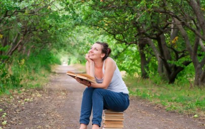 Lady sitting on pile of book holding a book