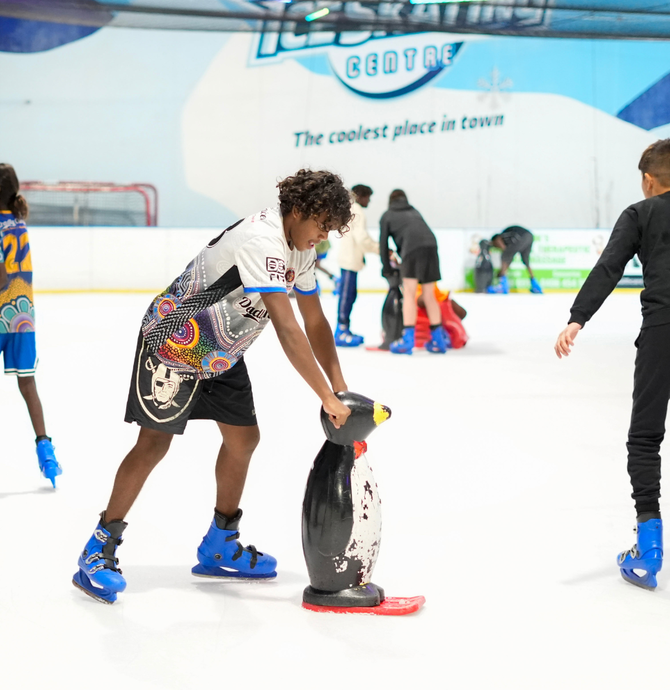 young person ice skating using plastic penguin as support aid