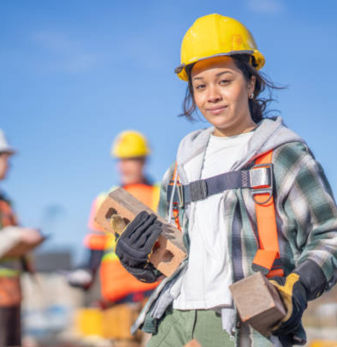 young woman with hard hat holding bricks on a construction site