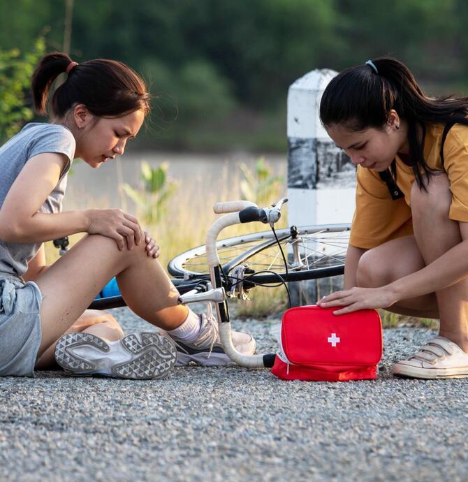 two young girls, one fallen off their bike, the other performing first aid