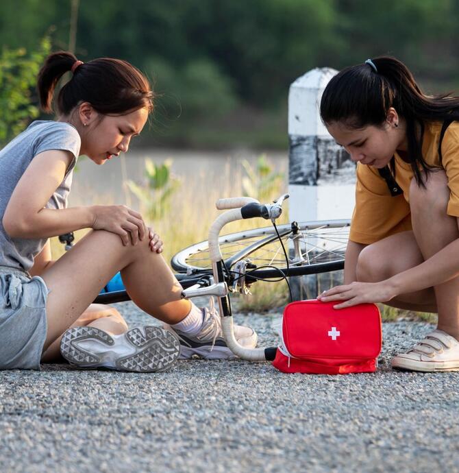 two young girls, one fallen off their bike, the other performing first aid