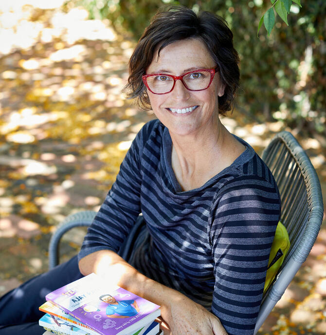 Author Deb Fitzpatrick sitting down with her books on a table.