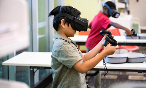 Two young boys play VR video games at the library together